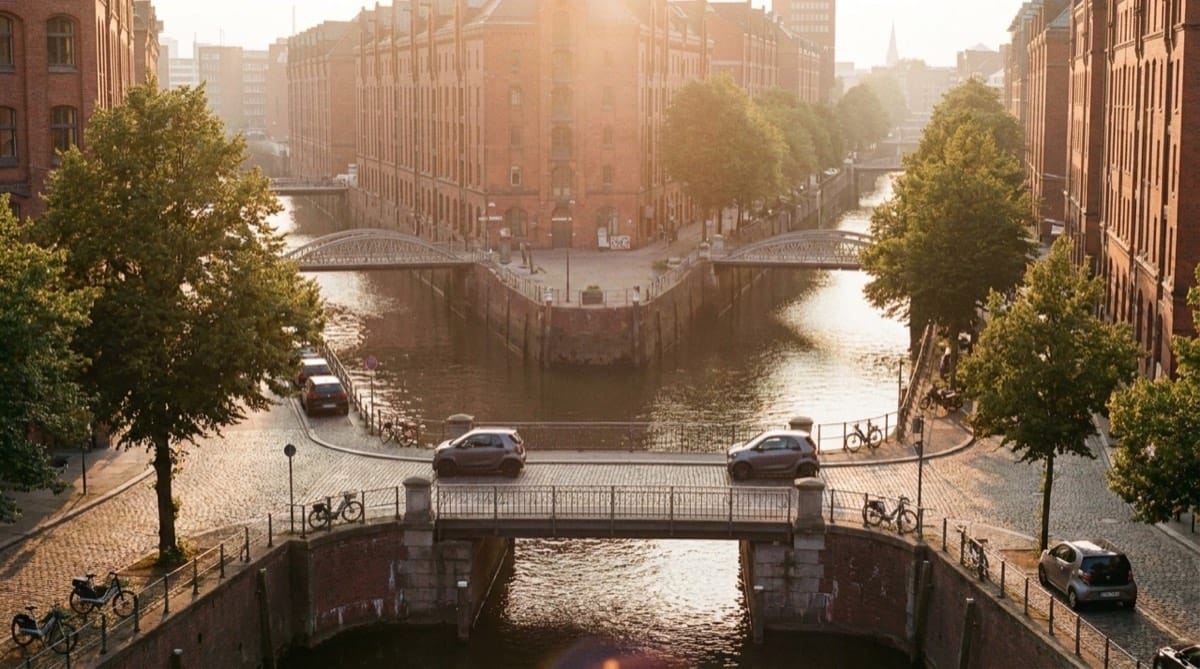 A golden-hour view over a European canal city with small electric cars crossing a bridge.