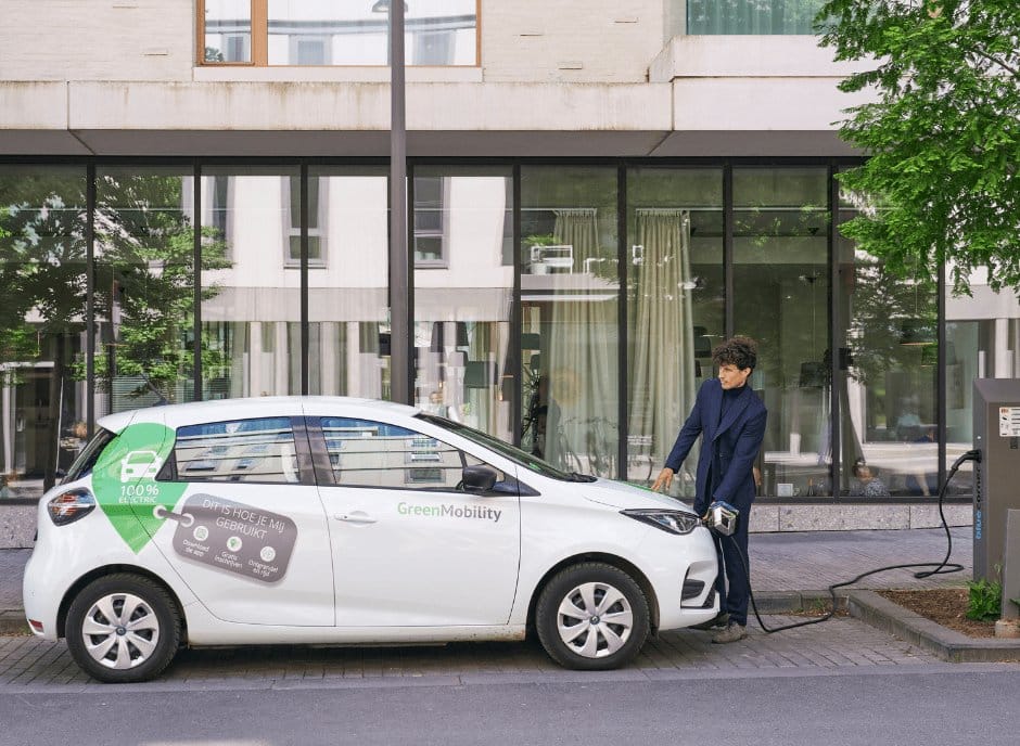 A driver plugging in a GreenMobility electric carsharing vehicle at a curbside charge point.